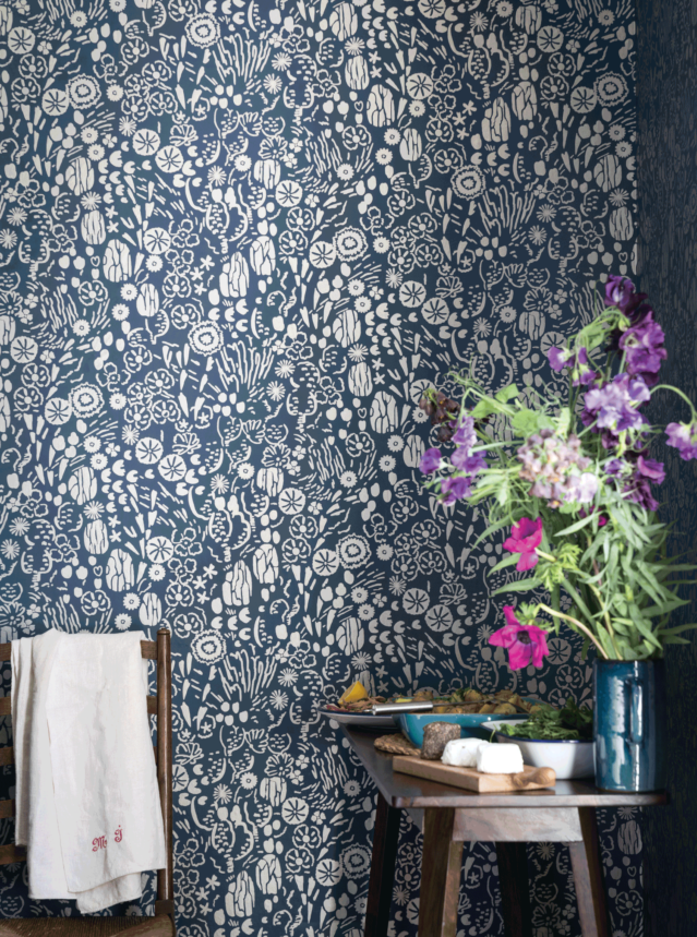 壁：FARROW&BALL 壁紙 5806 Atacama / ネイビーのベースカラーにさまざまな白の植物や花のデザインが施された壁面。手前にはタオルがかかったチェア、野花と食べ物がディスプレイされている小さなテーブルが置かれている。