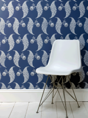 壁：FARORW&BALL 壁紙 1947 Rosslyn / ブルーの地色に上品な白の花の模様が施されている壁紙の前に、白いチェアが置いている。床も巾木も白で塗装されている。