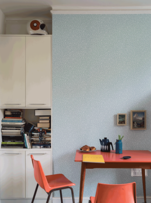 壁：FARORW&BALL 壁紙 5204 Blostma / 風に舞い散る花びらが一面にデザインされている淡く明るいブルーの壁紙の前に、赤系統のチェアとダイニングテーブルがあるダイニングキッチン。