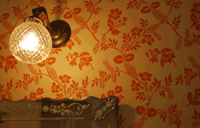 写真提供：株式会社ヤマダタッケン様 / 壁： FARROW&BALL 壁紙 1418 Melrose (Archive) / 白のベースカラーに、ソフトな赤系の花柄が施されている空間。電球色のオレンジの光に照らされて暖かな雰囲気に。