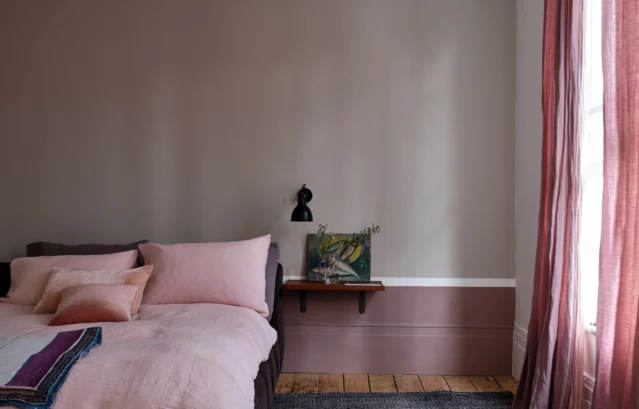 寝室 FARROW&BALL / 壁上部：No.229 Elephant's Breath / 壁下部：No.295 Sulking Room Pink / モールディング：No. 239 Wimborne White / ピンクや紫みを感じる顔料が含まれた落ち着いた色味の塗料で塗装されたベッドルーム。カーテンやベッドリネンも淡いピンクや赤紫系を使っており、ナチュラルシックな印象に仕上がっている。