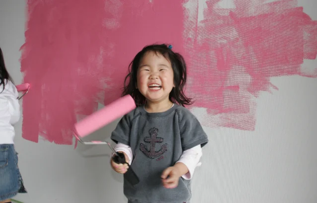 小さな女の子が、とても楽しそうに大きな笑顔でピンクの壁を塗っている最中の写真。 内装塗料に求められるのは「見た目の美しさ」だけでなく、子どもでも安心できる安全性で、毎日吸い込む空気への影響が少ないことが大前提です。 低VOC・低臭気の水性塗料が内装に選ばれる理由は、まさにここにあります。