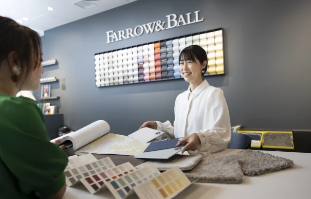 FARROW&BALL 銀座サロンでスタッフの女性が壁紙や塗装の色のご相談に対応している様子。不安定な情勢が続きますが、焦って購入をするのではなく、価格はもちろん、安全性や臭い、仕上がり、目的の空間や用途への適性も一緒に確認することが、長い目で見て「賢明な選び方」につながります。「こんな空間で過ごしたい」というご希望が明確になってきたら、お早めに私たちへご相談ください。